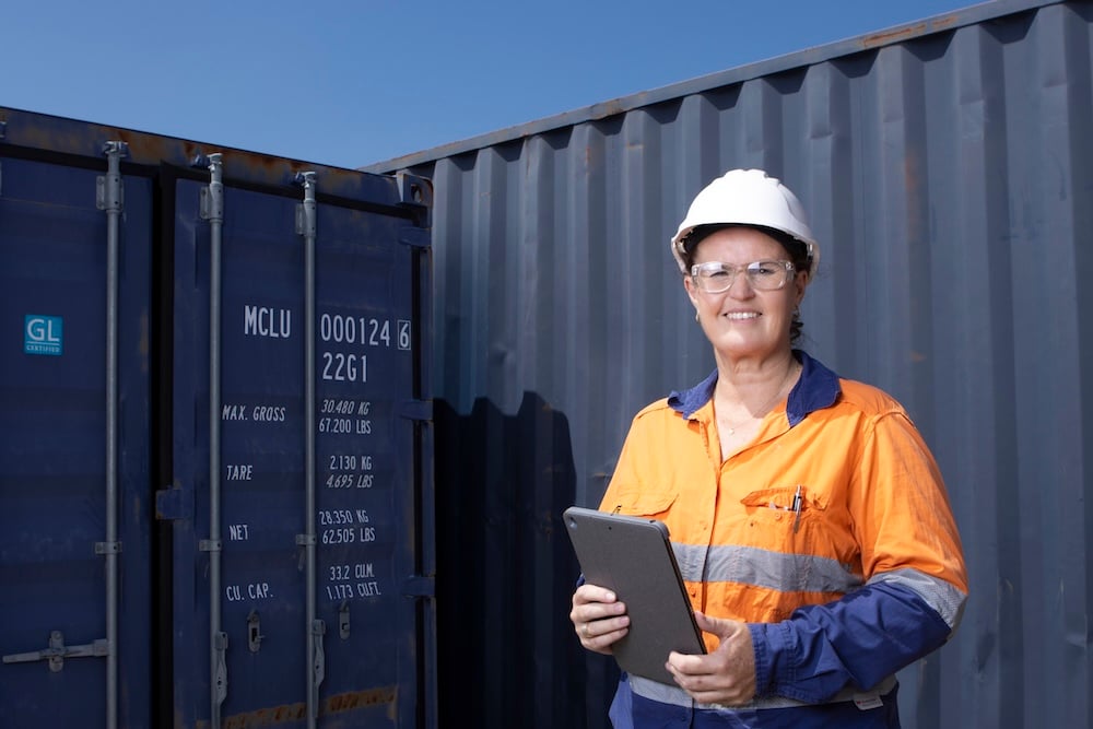 BSQC inspector in hi-vis gear holding a tablet standing in front of a sea container at a port facility