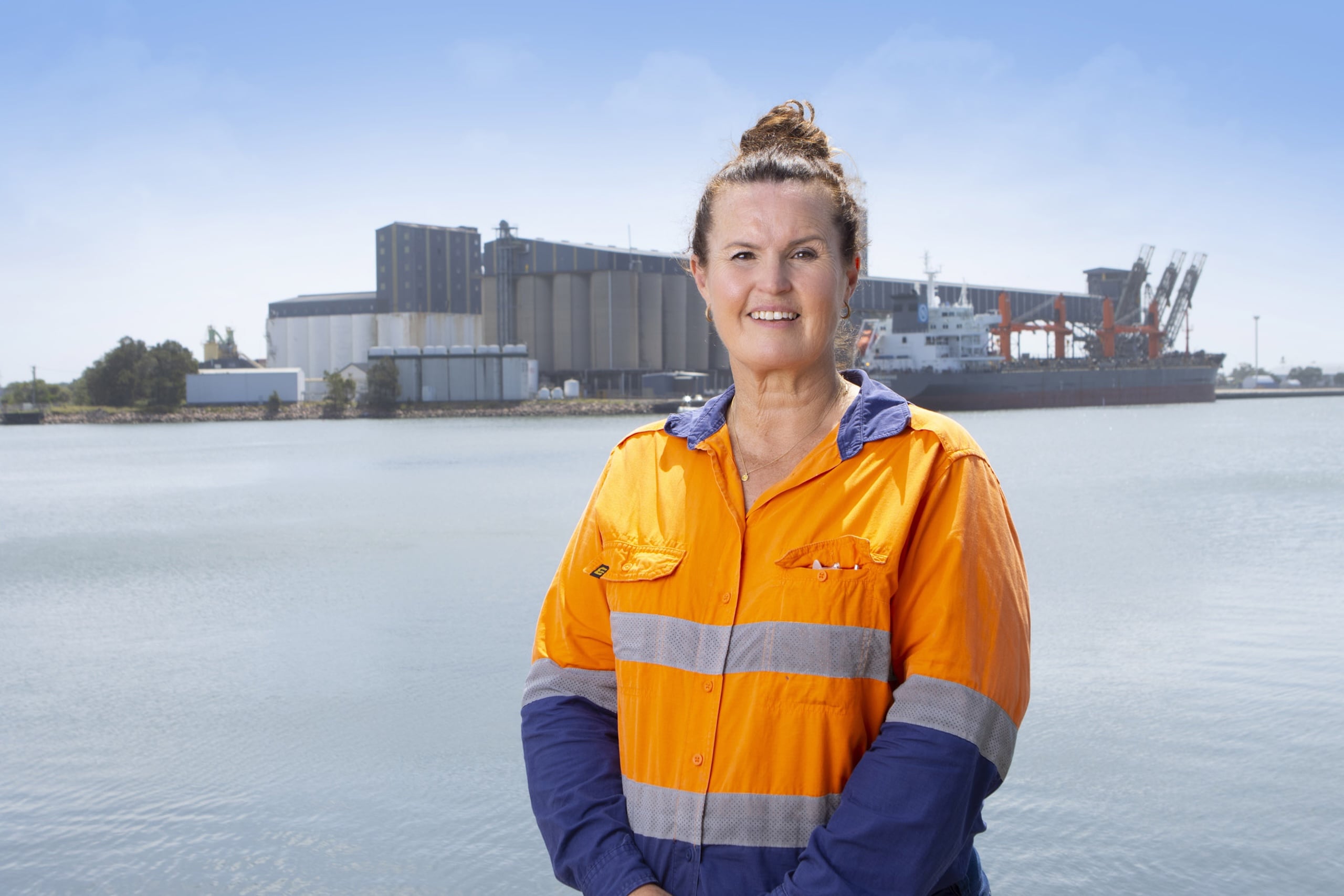Melanie McBlane, BSQC biosecurity consultant in hi-vis shirt standing at Newcastle port with grain silos and a cargo ship in the background